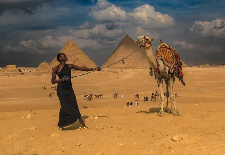 De verloren Afrikaanse beschaving die zelden wordt besproken 8 Een vrouw in een zwarte jurk houdt de leiband van een kameel vast in de buurt van de piramides van Gizeh, terwijl groepen mensen en kamelen op de achtergrond bewegen onder een bewolkte hemel, wat scènes oproept die zijn vormgegeven door automatische concepten.
