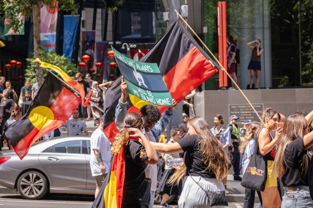 Hoe Europa Afrika echt onderontwikkelde: de waarheid die niet werd onderwezen 3 Een groep mensen met vlaggen en borden van Aboriginals en Torres Strait Islanders verzamelt zich in een straat tijdens een protest of rally overdag, waarbij de nadruk wordt gelegd op de connecties tussen inheemse rechten in Australië en bewegingen in Afrika en Europa.
